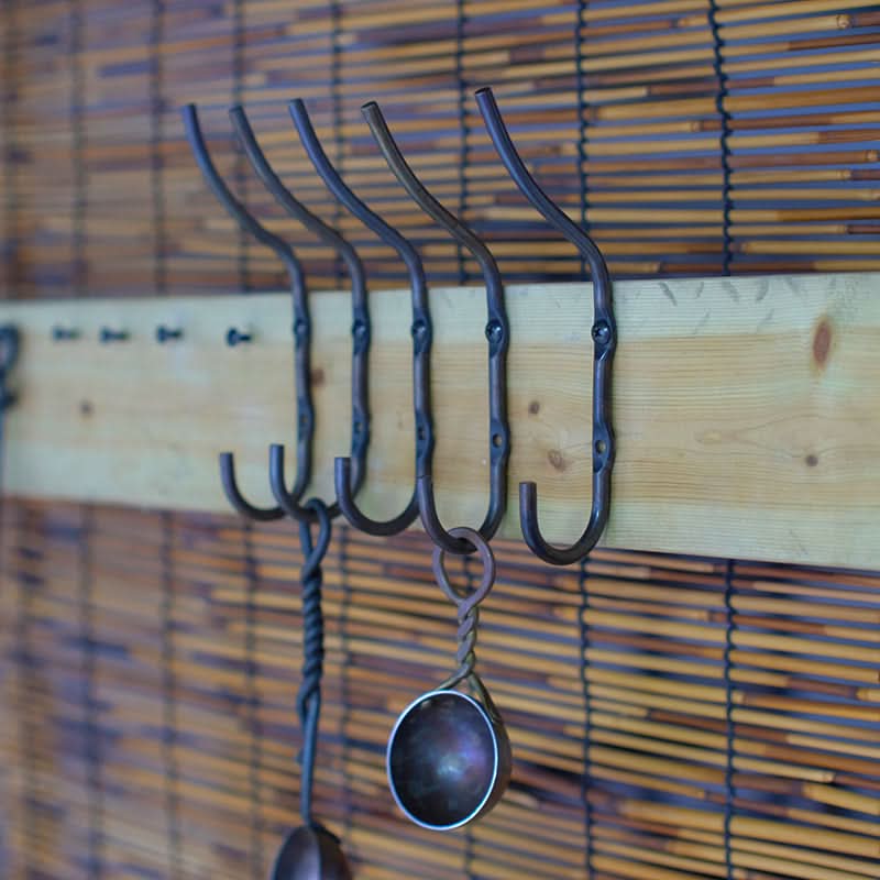 Rustic wall hooks - hand forged iron hooks with decorative spoons, on wooden plank against bamboo backdrop.